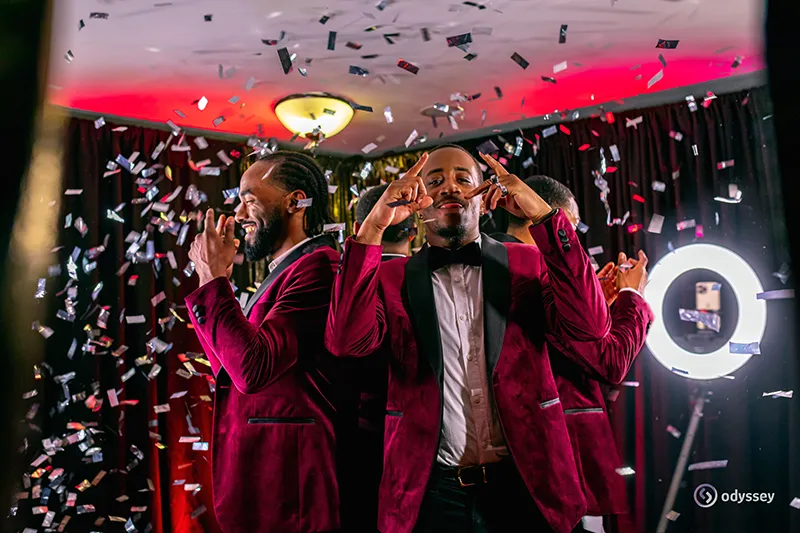 Guests in burgundy velvet jackets celebrating beneath falling confetti at an Odyssey Events photo experience